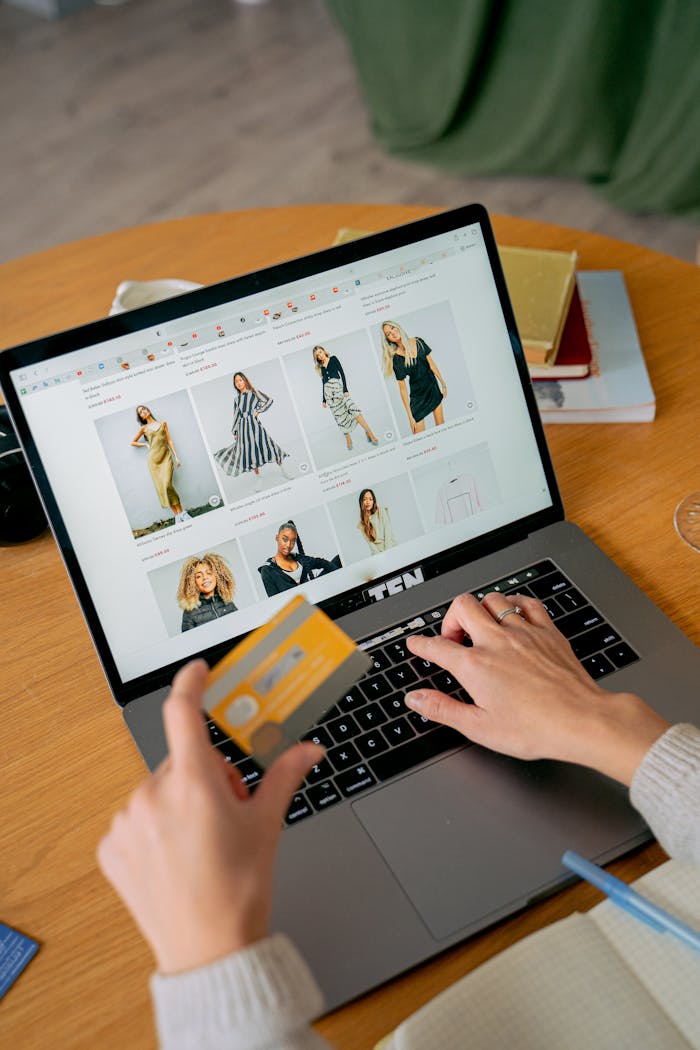 ours-journey A woman makes an online purchase using a credit card on her laptop, browsing an online fashion store.