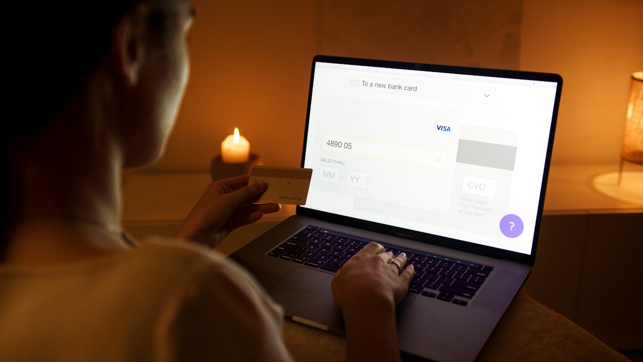 gallery-5 A woman makes a secure online payment using a laptop and credit card in a cozy setting.