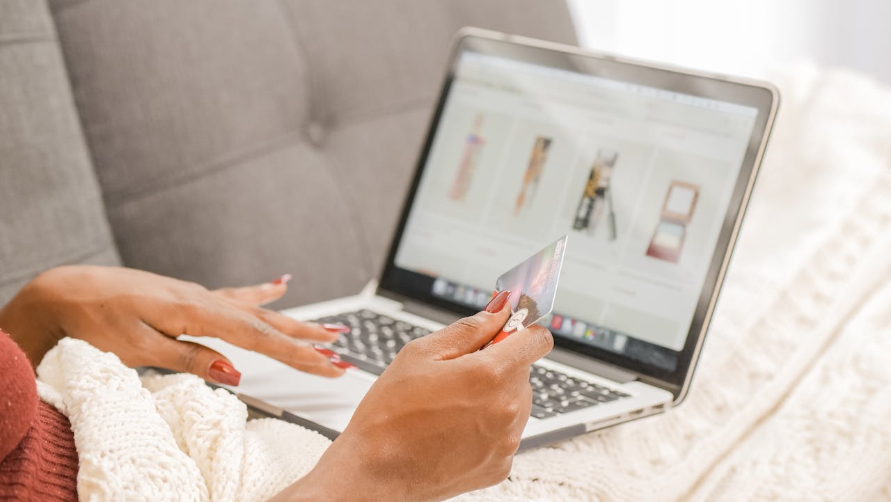 gallery-4 A woman relaxes on a couch while shopping online using her laptop and credit card.